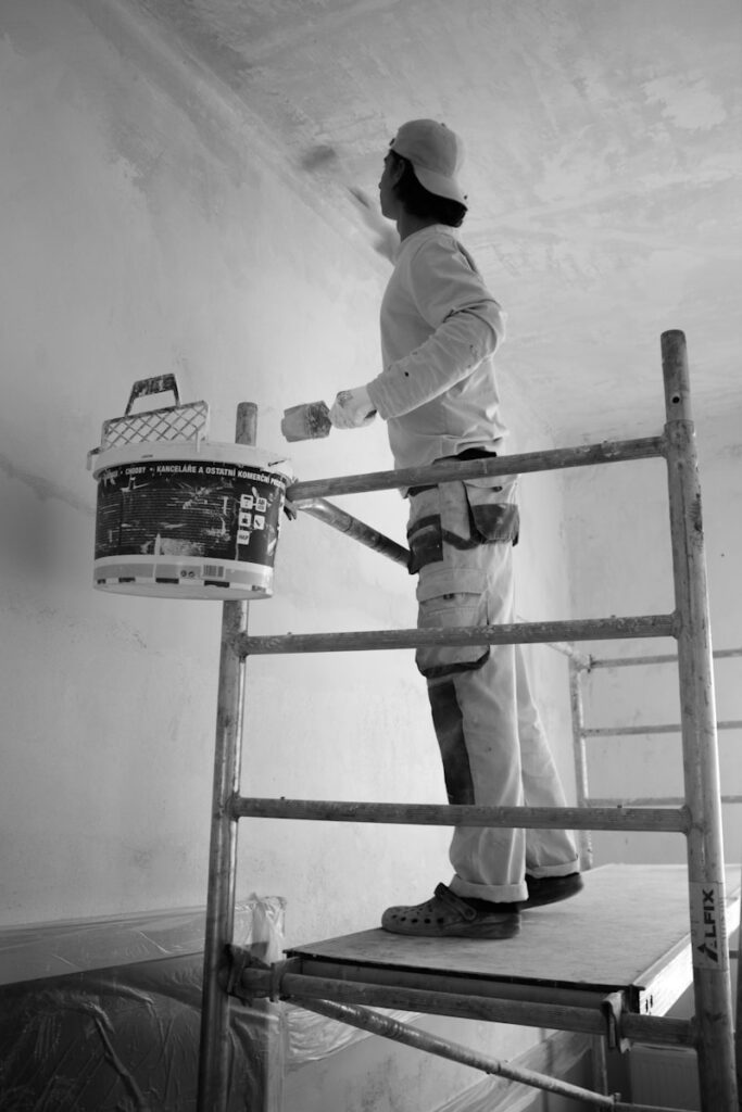 Handwerker auf Gerüst, streicht Decke in Innenraum. Effiziente Renovierung für ein perfektes Finish.