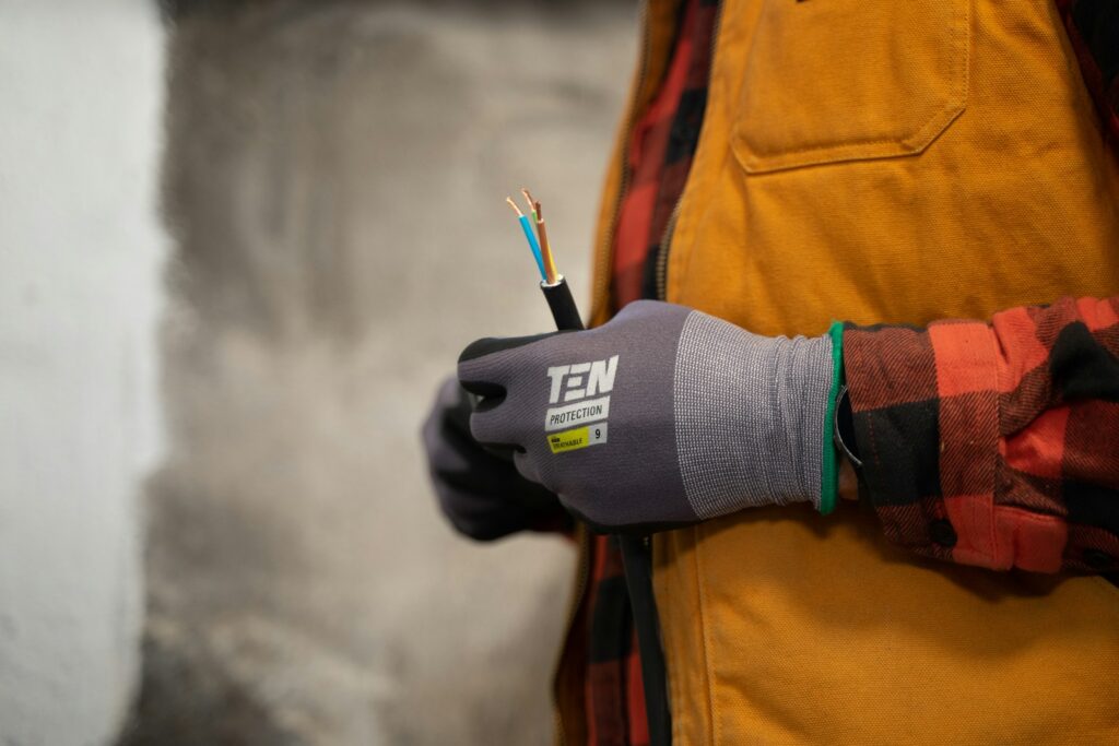 Elektriker mit Handschuhen hält Stromkabel in Werkstattkleidung. 7zwo MEDIA – Ihr Partner für innovative Werbung.